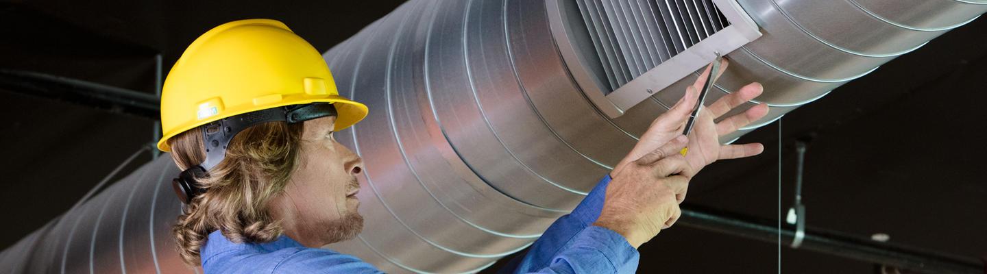 Man with yellow hardhat working on an air vent